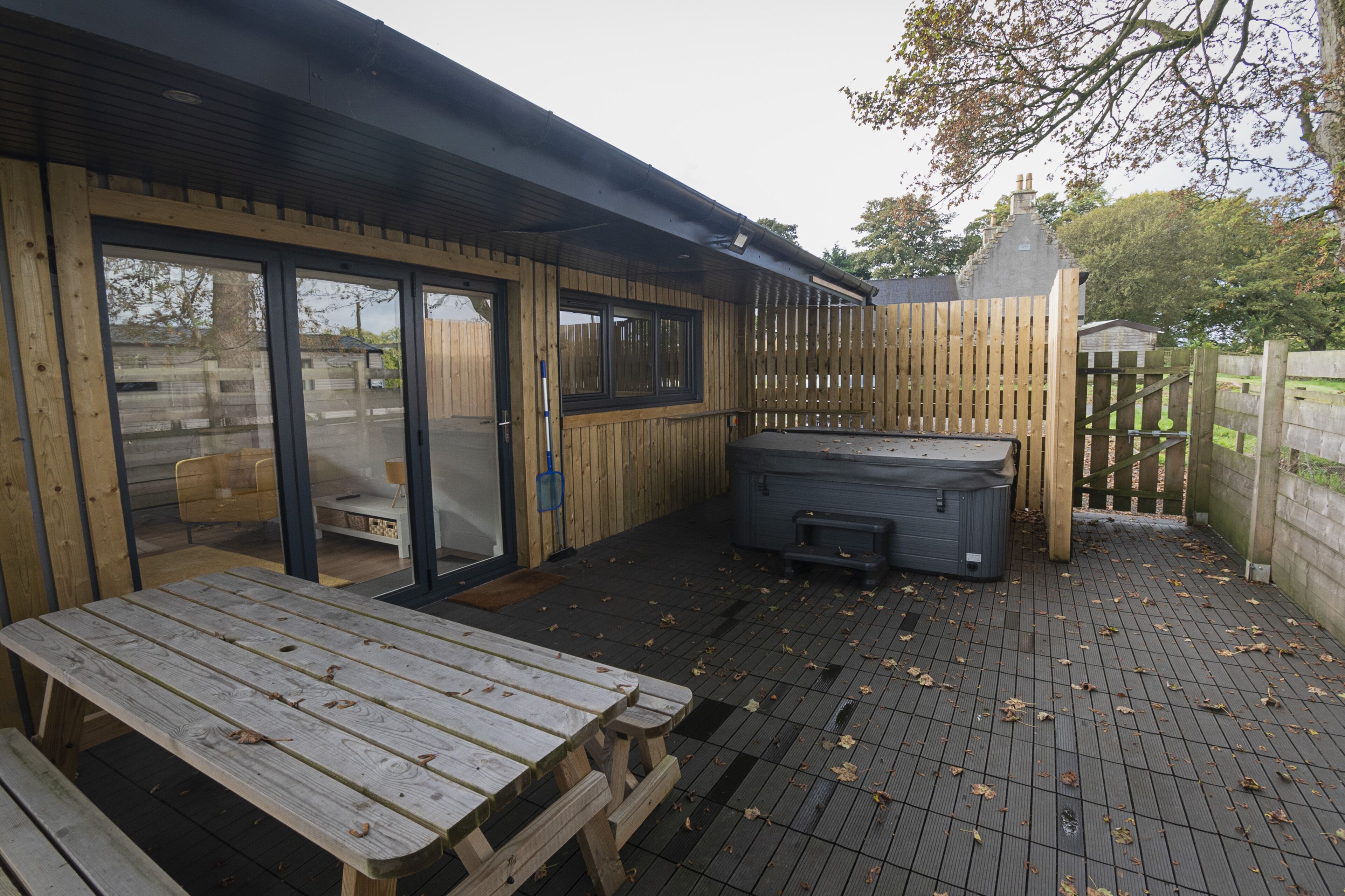 A wooden deck with a hot tub, picnic table, and sliding glass doors leading to an indoor area.