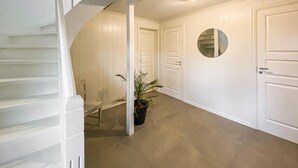 En gang med trappe, hvide døre og en potteplante.