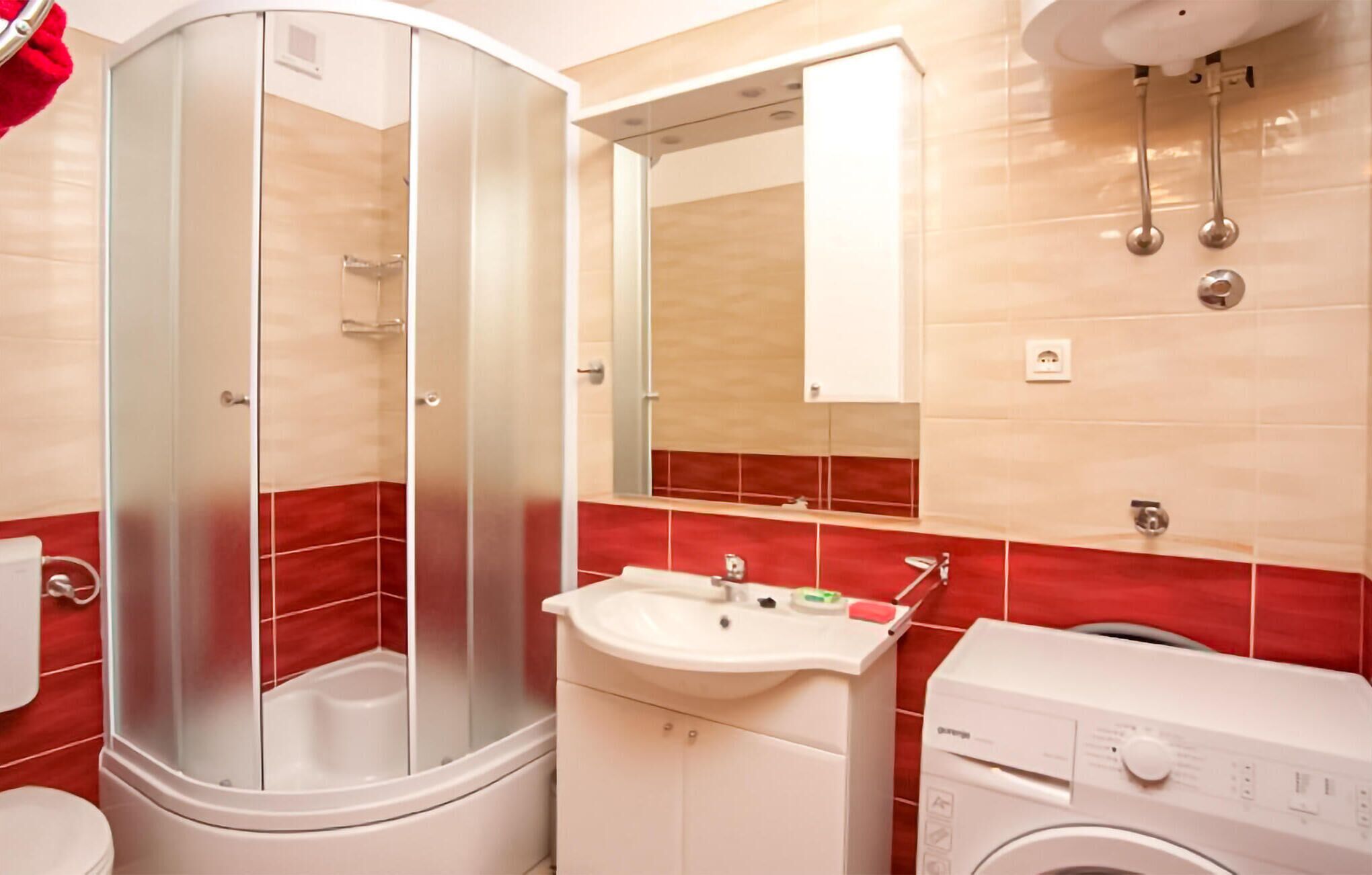 A bathroom with a glass-enclosed shower, a sink, a mirror, and a washing machine.