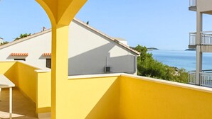 Ein gelber Balkon mit Blick auf das Meer und ein Gebäude mit rotem Ziegeldach.