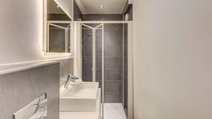 Un bagno con un lavandino bianco, uno specchio e una zona doccia.