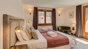 Una camera d'albergo con un letto grande, una poltrona verde, un comodino con una lampada e una finestra con tende.