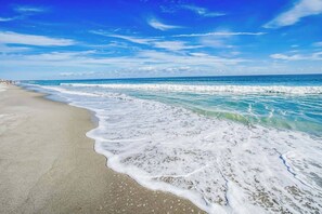 A beach with waves gently lapping at the shore under a clear blue sky. - Prime Space Coast Location! 2BR Oceanfront, Pool, Hot Tub, Tiki Bar at Discovery Beach Resort! (Cocoa Beach)