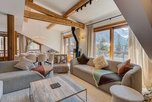 Een gezellige woonkamer met een hoge plafond, houten balken, een open haard en grote ramen met uitzicht op de bergen.