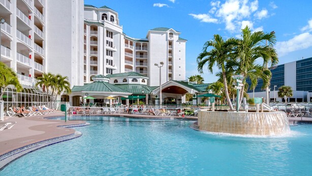 Un hotel con una piscina grande, palmeras y un edificio moderno con varios balcones.