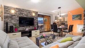 A modern living room with a stone wall, a flat-screen TV, and a dining area with a table and chairs. - Gorgeous apartment in Rijeka with house sea view (Rijeka)
