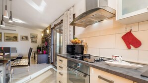 A modern kitchen with stainless steel appliances, a dining area with a table and chairs, and a red oven mitt on the wall. - Gorgeous apartment in Rijeka with house sea view (Rijeka)