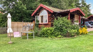 A wooden cabin with a red roof, surrounded by a well-maintained garden and a wooden fence.