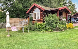 A wooden cabin with a red roof, surrounded by a well-maintained garden and a wooden fence. - Beautiful home in Botolfsbo with sauna (Botolfsbo)