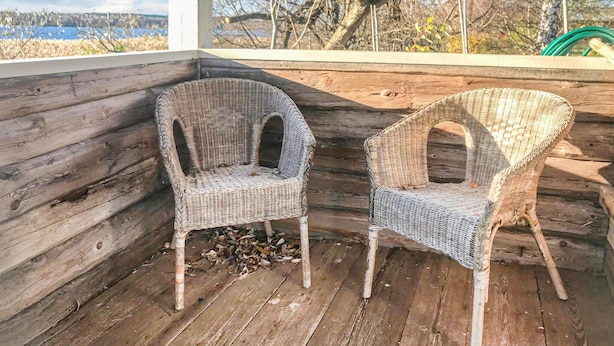Two wicker chairs on a wooden deck with a view of a body of water and trees in the background.