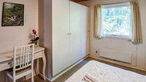 Une chambre à coucher comprenant un lit, un bureau avec une chaise, une armoire, une fenêtre avec des rideaux et un radiateur.