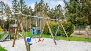 Une aire de jeux avec des balançoires, un toboggan et un petit abri bleu.