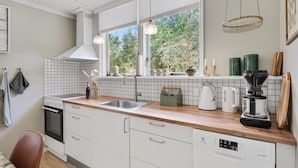 A modern kitchen with white cabinets, a wooden countertop, a built-in oven, and a window with a view of greenery. - Beautiful home in Aakirkeby with WiFi (Aakirkeby)