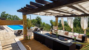 Un'area salotto all'aperto coperta, con piscina e vista sul mare.