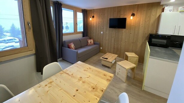 Un espace de vie compact comprenant un mur en bois, un canapé, un téléviseur, une table à manger et un coin cuisine.