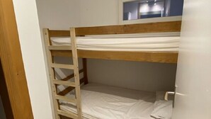 Une chambre avec un lit superposé, une échelle en bois, du linge de lit blanc et une fenêtre située au-dessus du lit supérieur.