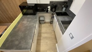 Une cuisine de taille réduite avec des meubles blancs, un plan de travail noir et une machine à café.