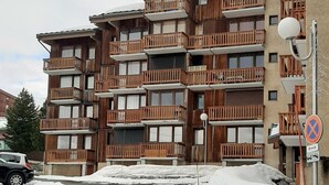 Un immeuble en bois à plusieurs étages, doté de balcons, d’un mur en pierre et d’un sol recouvert de neige.