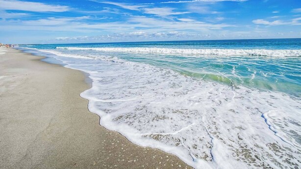 Een strand met golven die zachtjes op de kust komen, onder een helderblauwe lucht.