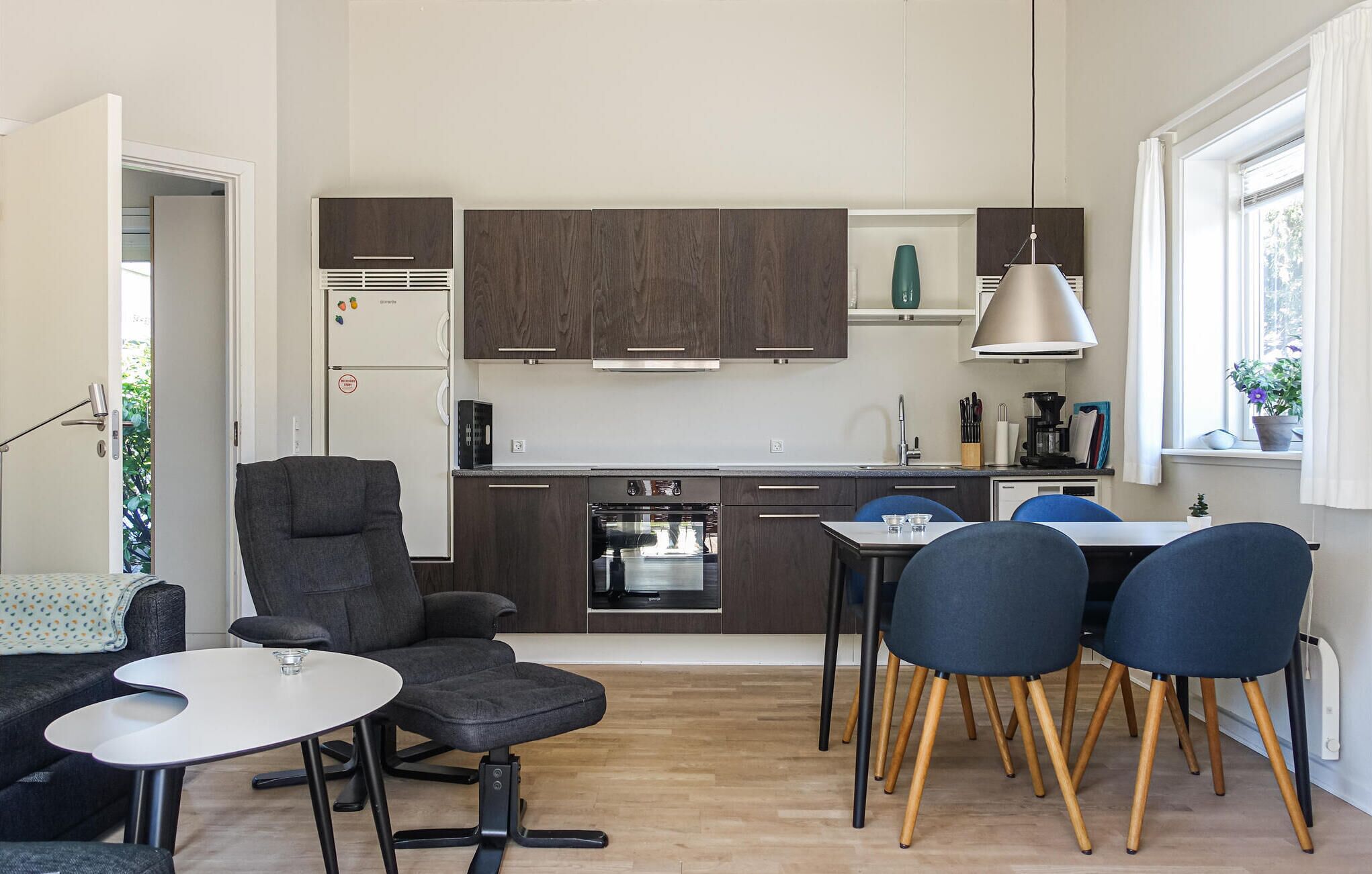 A modern kitchen with dark wood cabinets, a built-in oven, and a dining area with a round table and four chairs.