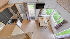 Una cuina compacta amb forn i microones integrats, zona de menjador amb taula i caires, i un gran finestral que ofereix vista a l'exterior.