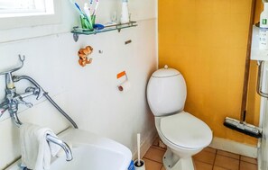 Une salle de bain avec un lavabo blanc, des toilettes et un espace douche. On y trouve une étagère avec des articles de toilette et une petite figurine accrochée au mur.