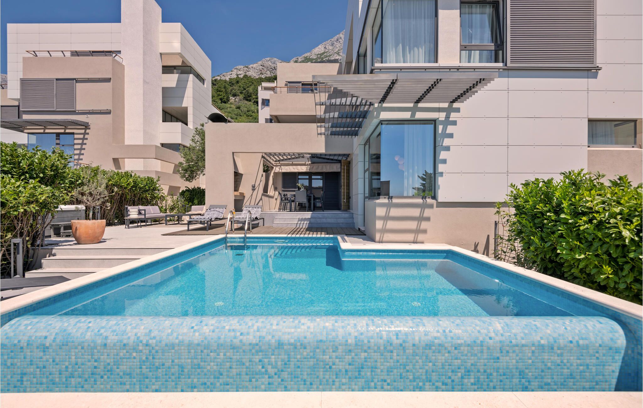 Un espace piscine moderne avec une piscine à l’eau d’un bleu limpide, entourée de chaises longues et de plantes en pot.