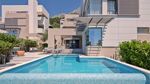 A modern pool area with a clear blue pool, surrounded by lounge chairs and potted plants. - Luxurious home in Makarska with sauna (Makarska)