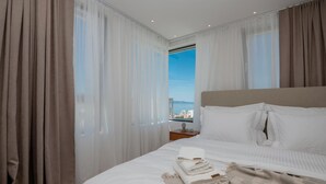 A hotel room with a large bed, white linens, a view of the city, and sheer curtains. - Luxurious home in Makarska with sauna (Makarska)
