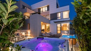 A modern outdoor hot tub area with a pool, surrounded by lush greenery and a contemporary building with large windows. - Luxurious home in Makarska with sauna (Makarska)