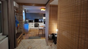 A narrow hallway leading to a kitchen with a dining area, featuring a patterned rug, a radiator, and a trash bin.