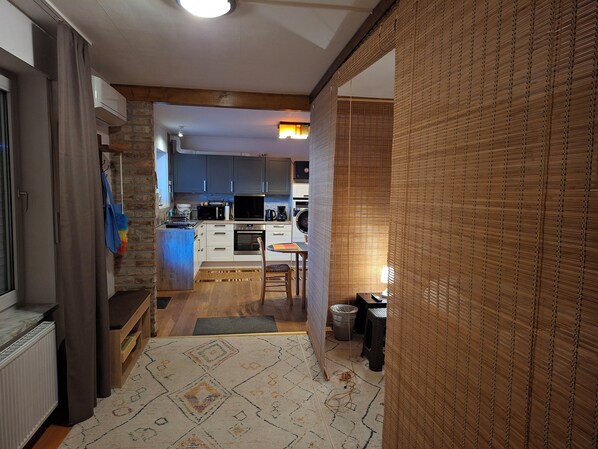 Un couloir étroit mène à une cuisine dotée d’un coin repas, où l’on trouve un tapis à motifs, un radiateur et une poubelle.