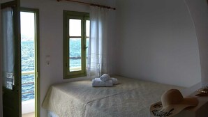 A bedroom with a bed, a window with a view of the sea, a wooden ceiling, and a hat on the wall. - Milos By The Sea – Seafront House (Milos)