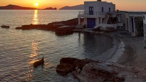 A coastal scene with a building near the water, a clear sky, and the sun setting or rising. - Milos By The Sea – Seafront House (Milos)
