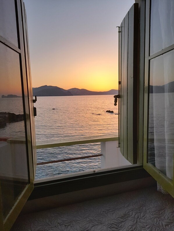 A room with a view of a sunset over a body of water, a balcony, and a patterned carpet.