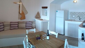 A cozy kitchen with a wooden table, white chairs, a sofa with striped cushions, a refrigerator, and a tiled backsplash. - Milos By The Sea – Seafront House (Milos)