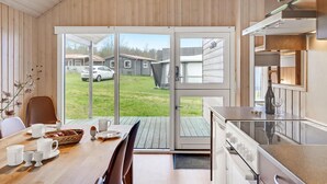 Eine moderne Küche mit einem großen Fenster, einem Essbereich mit Tisch für zwei Personen und Blick auf eine Wohngegend.