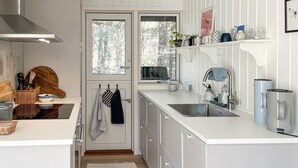 Une cuisine moderne avec des meubles blancs, un évier en acier inoxydable et une fenêtre donnant sur une forêt.
