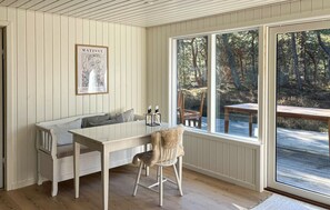 Una habitación acogedora con un banco de madera blanca, una mesa y una silla. Hay una obra de arte enmarcada en la pared y una ventana con vistas a árboles.