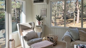 Une pièce chaleureuse avec une grande fenêtre, un fauteuil confortable, une petite table et un panier en osier.