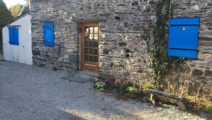 A stone building with a wooden door and blue shutters.
