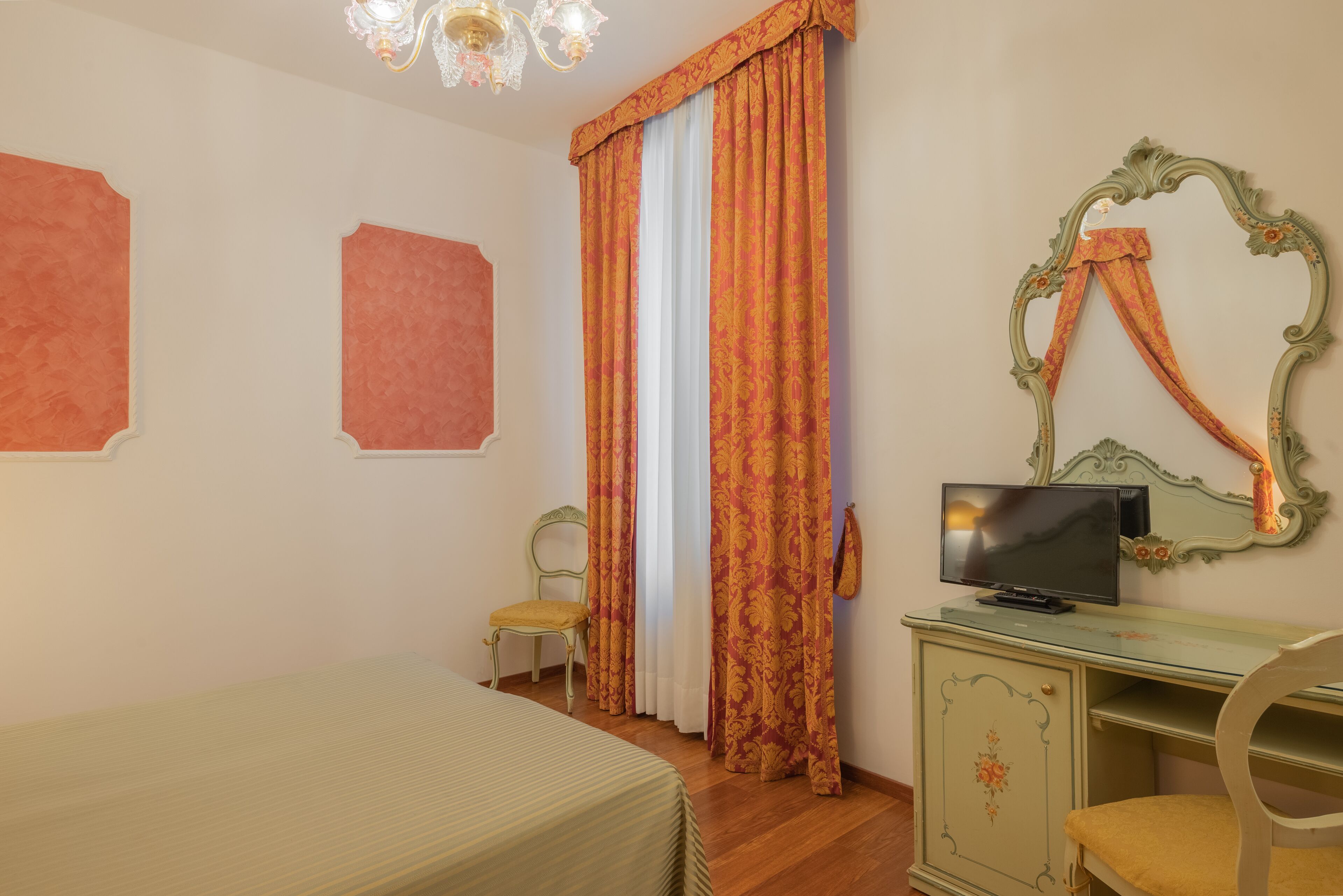 A bedroom with a bed, a desk with a television, two chairs, and a mirror.