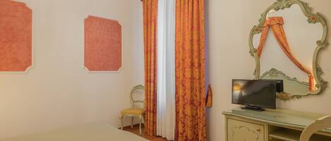 A bedroom with a bed, a desk with a television, two chairs, and a mirror.