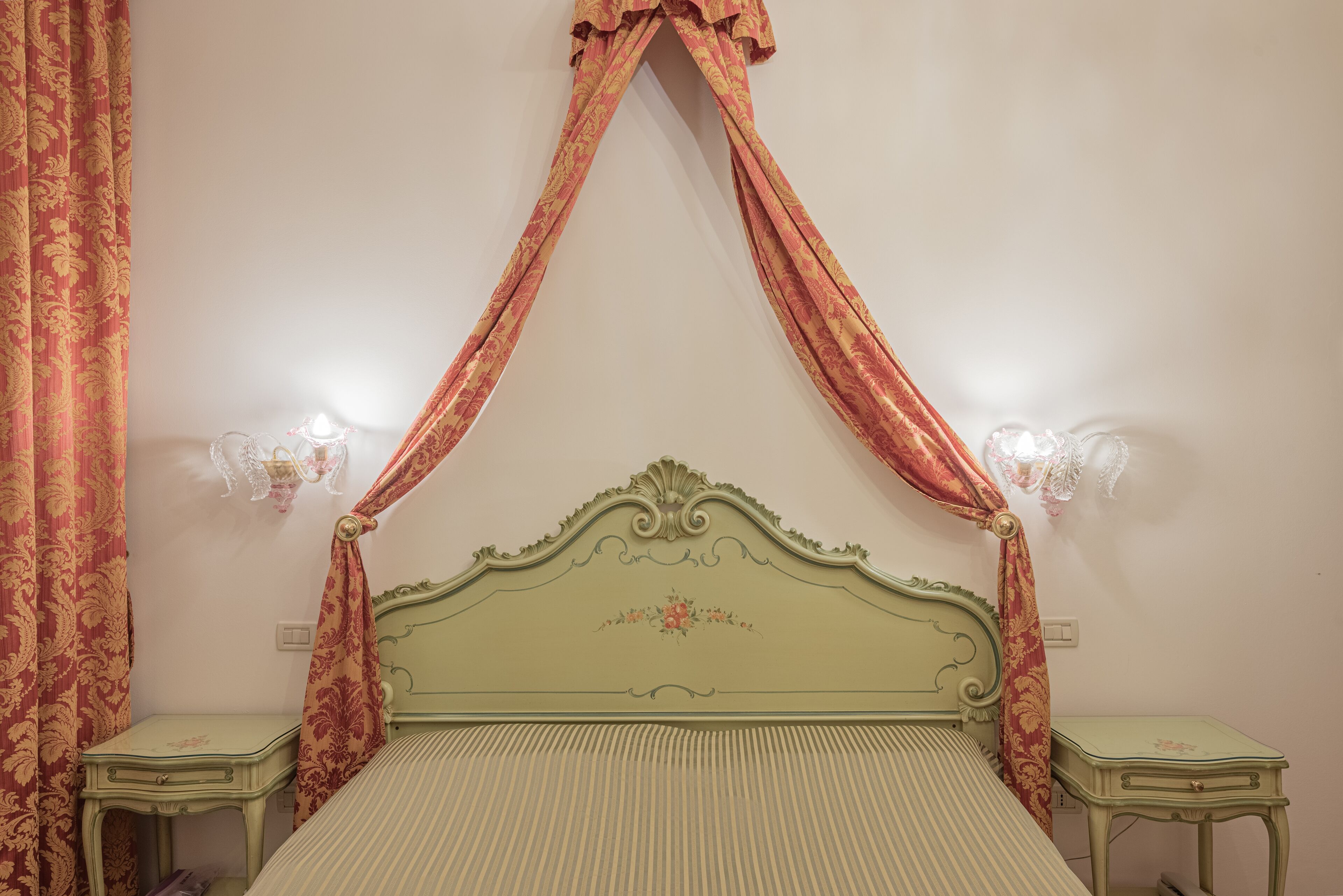 Un dormitorio con cama a dosel, dos mesitas de noche y una lámpara fijada a la pared.