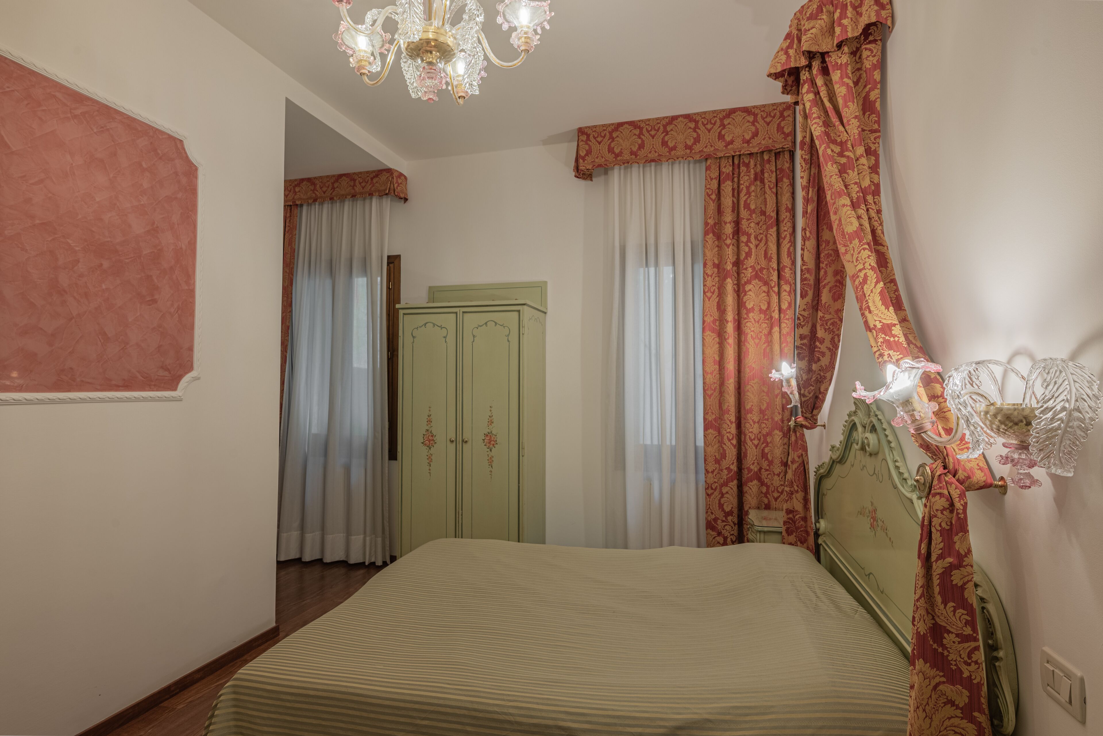 A bedroom with a bed, a green wardrobe, a chandelier, and curtains.