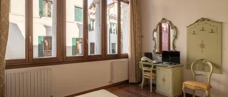 A room with large arched windows, a wooden floor, a desk with a chair, a television, and a green vanity with a mirror.