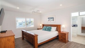 Quarto com cama de madeira, mesa de cabeceira, escrivaninha e ventilador de teto.