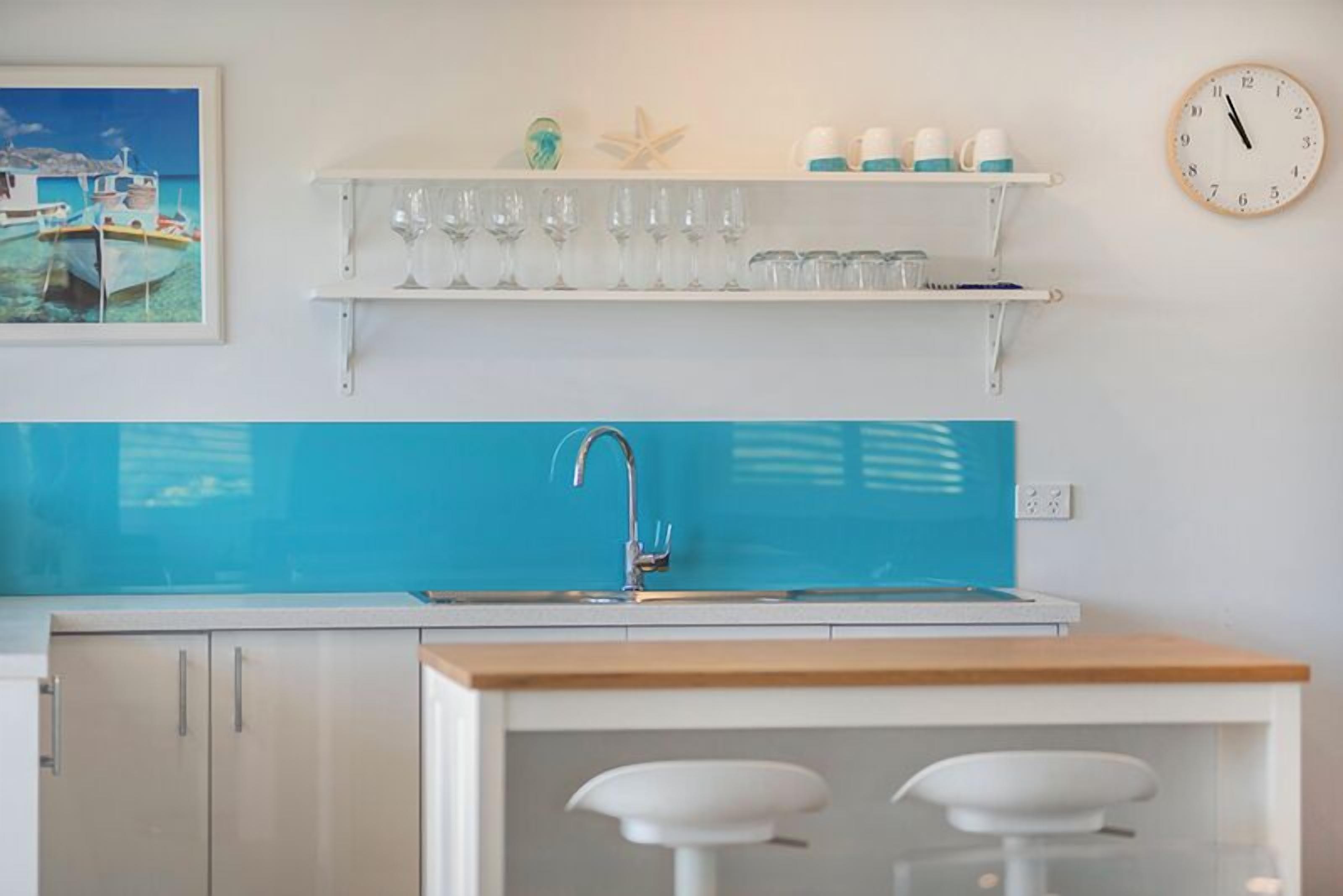 A kitchen with a blue backsplash, white cabinets, a wooden countertop, and a bar area with stools.