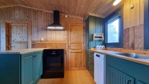 Una cocina compacta con paredes de madera, horno empotrado, lavavajillas y ventana que proporciona luz natural.