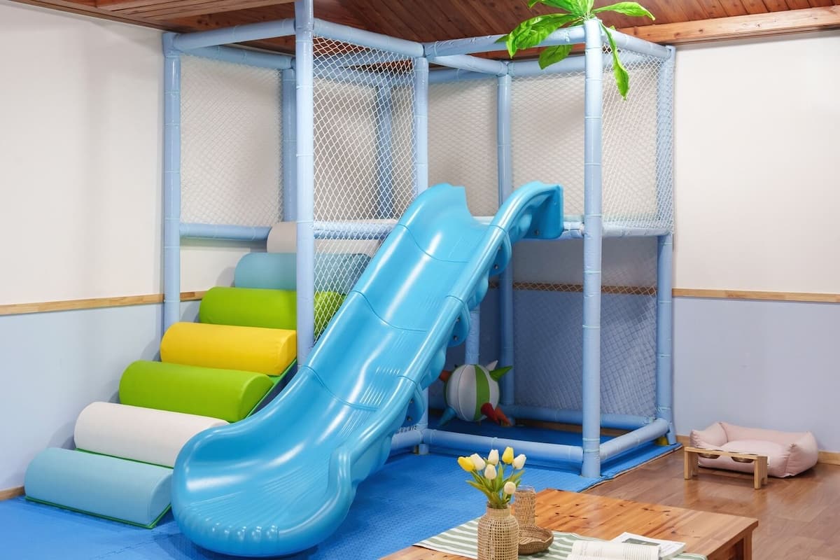 A play area with a blue slide, cushioned steps, and a netted enclosure.